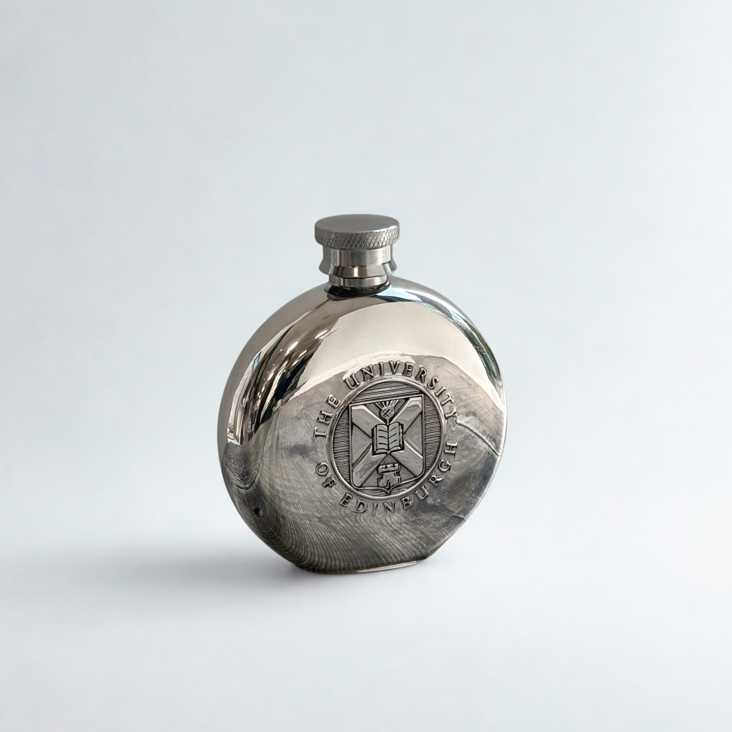 Front view of the round pewter hipflast with the embossed University crest visible.
