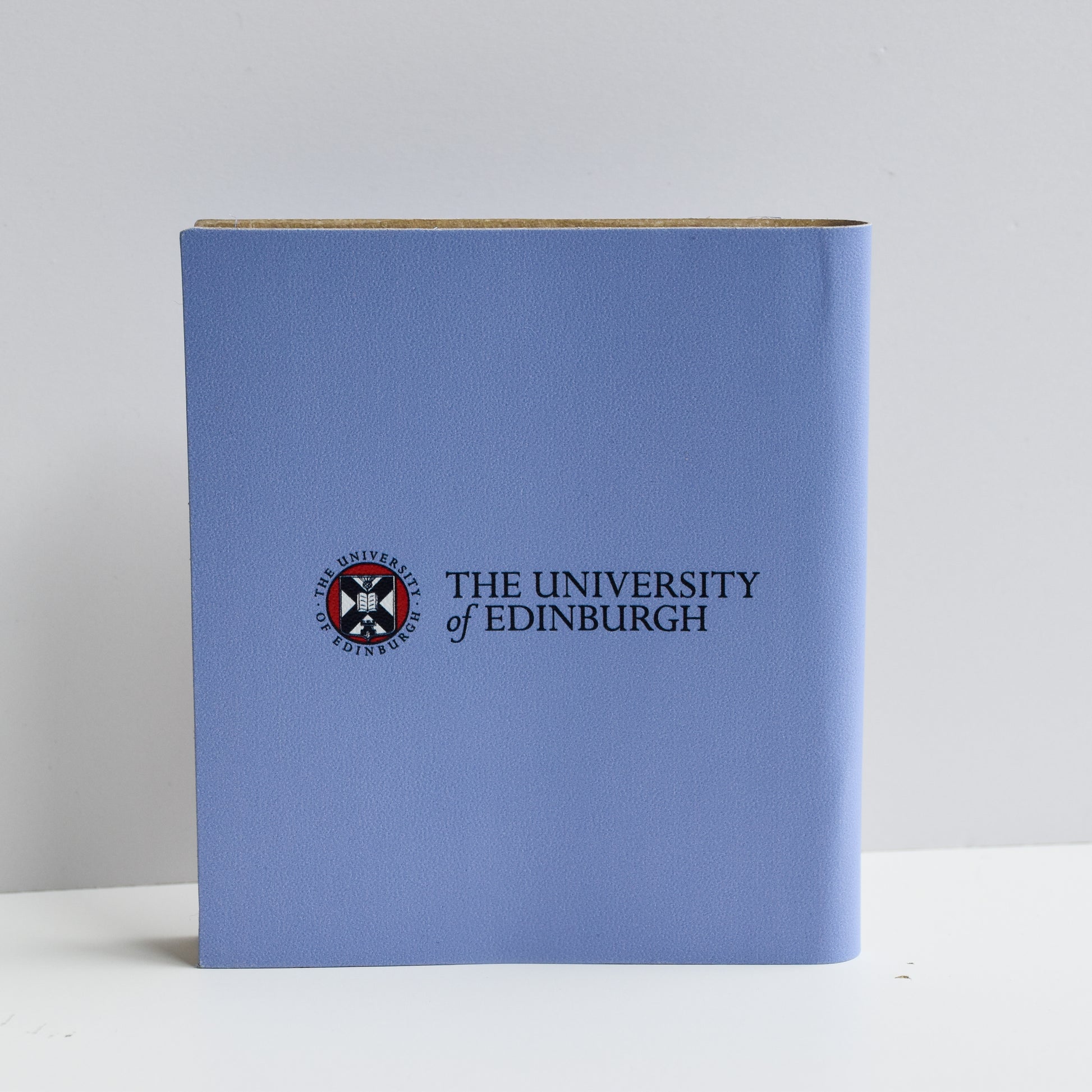 A close up of the Graduation Day Notebook back cover. It is blue with the University of Edinburgh crest, and 'The University of Edinburgh' in black text to the right of it in the centre of the cover.