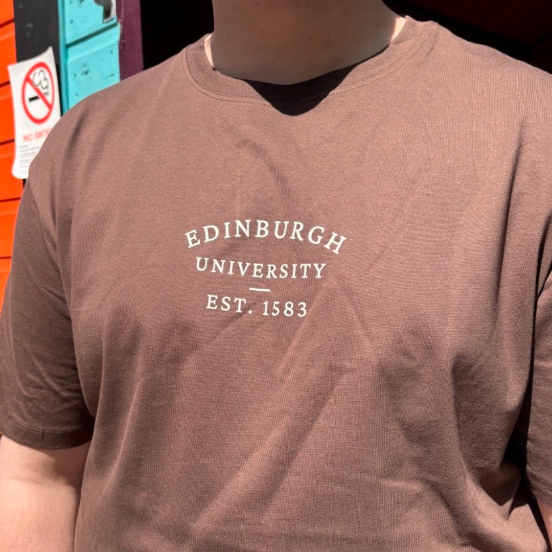 Person wearing brown Everyday t-shirt with 'Edinburgh University EST. 1583' printed on it.