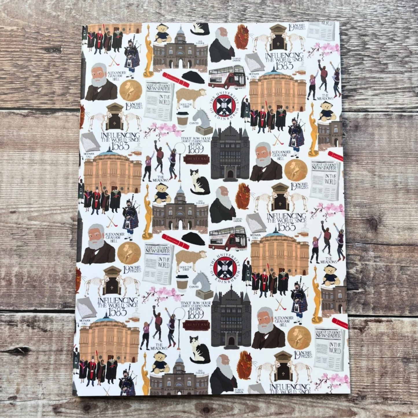 A close up of the A4 Heritage Collection notebook. It is white with various illustrated figures and images associated with the University of Edinburgh. Illustration by Designed by Esther.