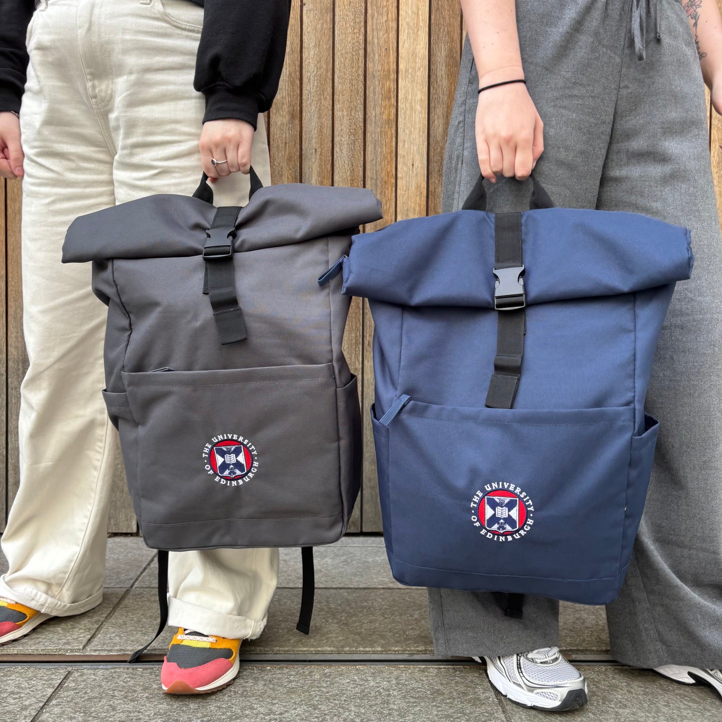 Models carry Classic roll top backpack in graphite and navy. Both backpacks feature a full coloured embroidered University Crest.