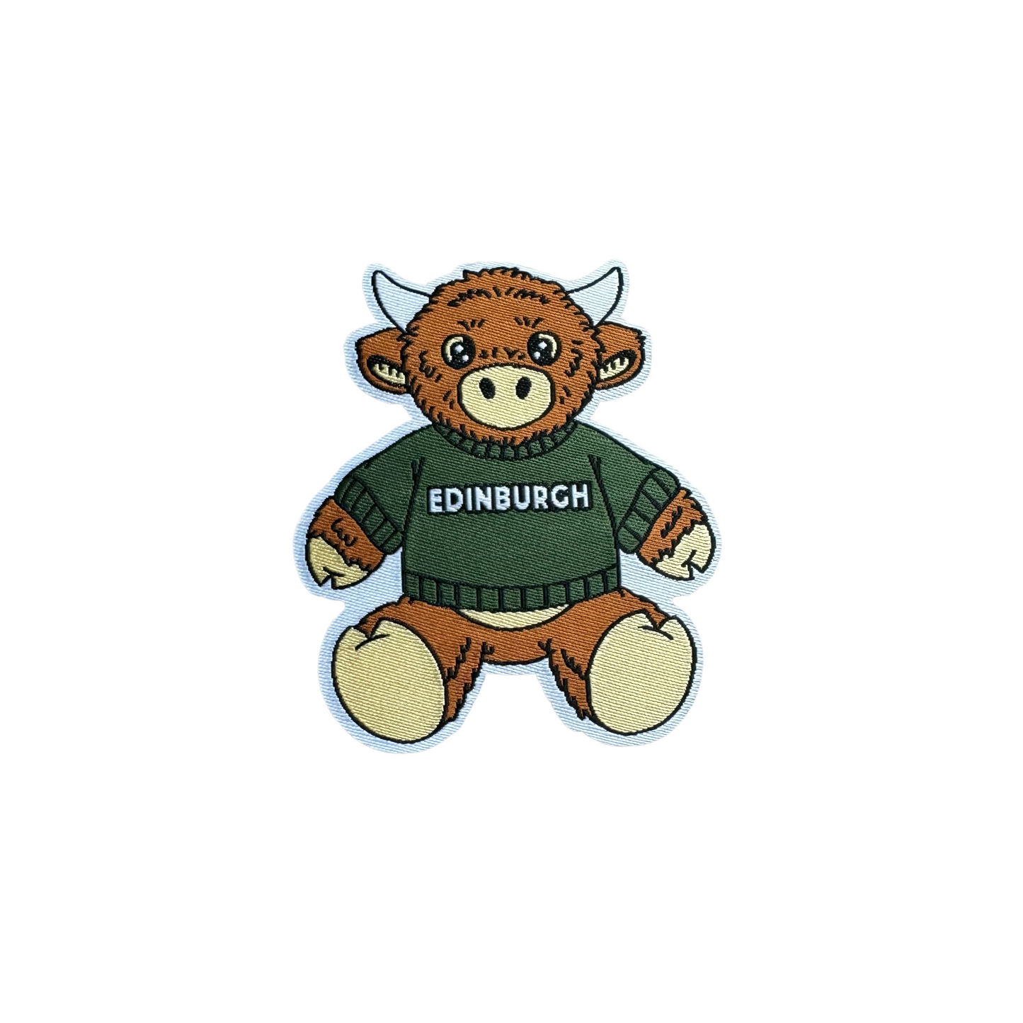 Close up of McCoowan Cow patch on a white background. McCoowan is redish-brown in colour and wearing a green sweater that says 'Edinburgh'.