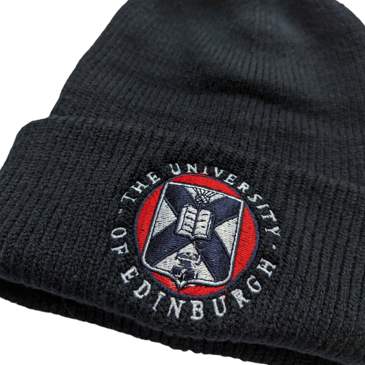 close up of navy ribbed cotton beanie with red, white and navy embroidered university crest