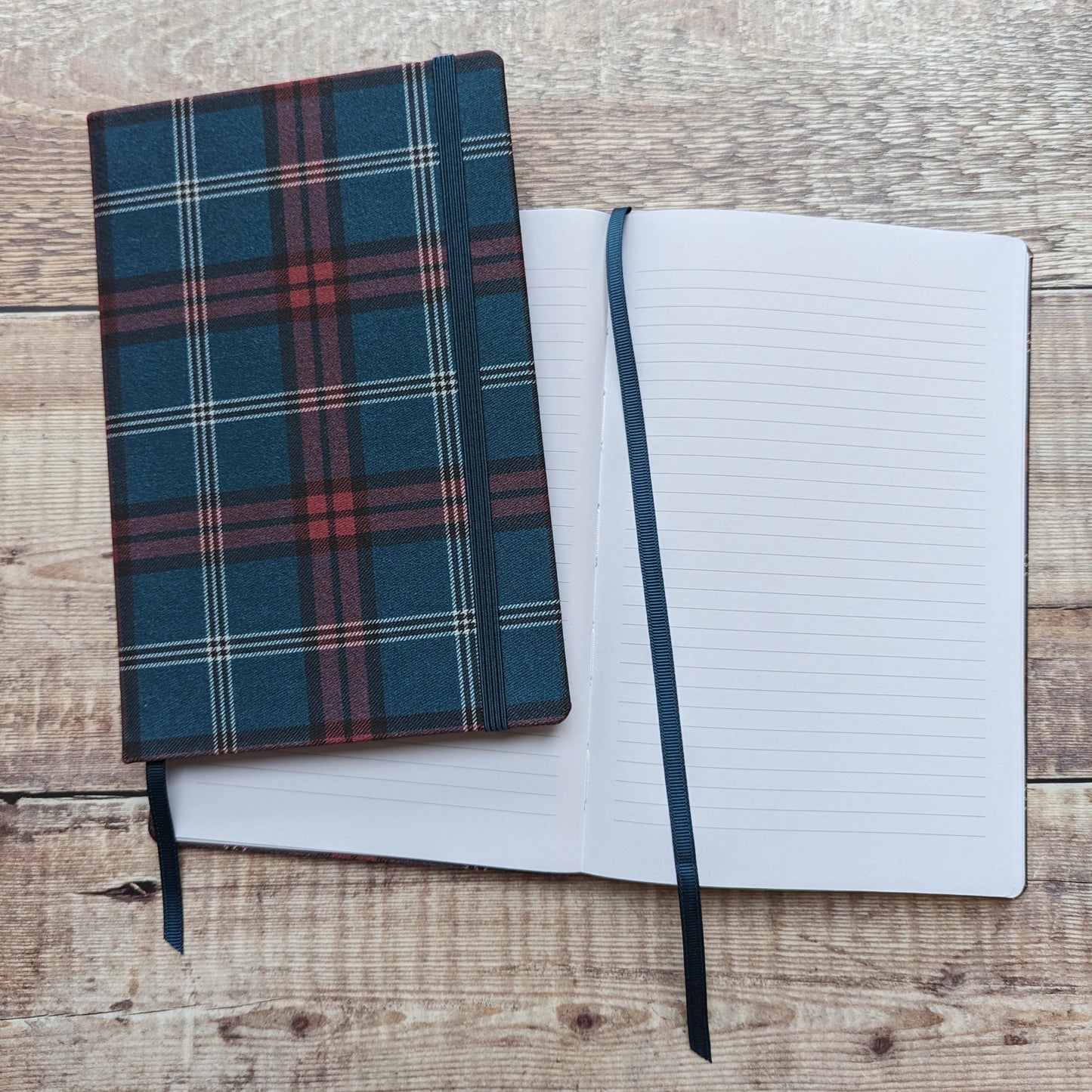 Two cloth-bound tartan notebooks. One is open displaying the full lined pages and ribbon bookmark.