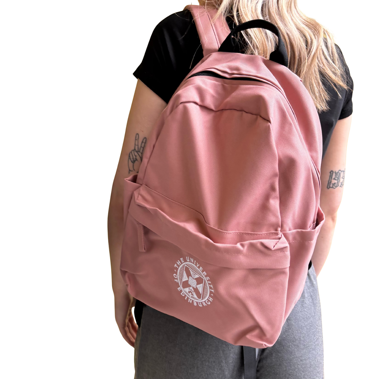Model wears the Mini Recycled Crest Backpack in rose pink featuring the University crest embroidered in white.