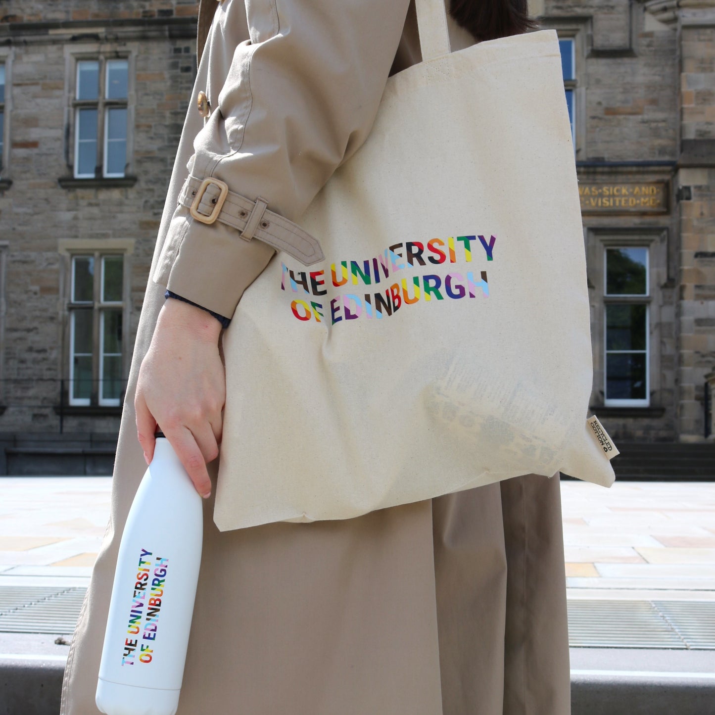 Model carries Pride Tote Bag and Edinburgh Pride Water Bottle in front of Edinburgh Futures Institute.