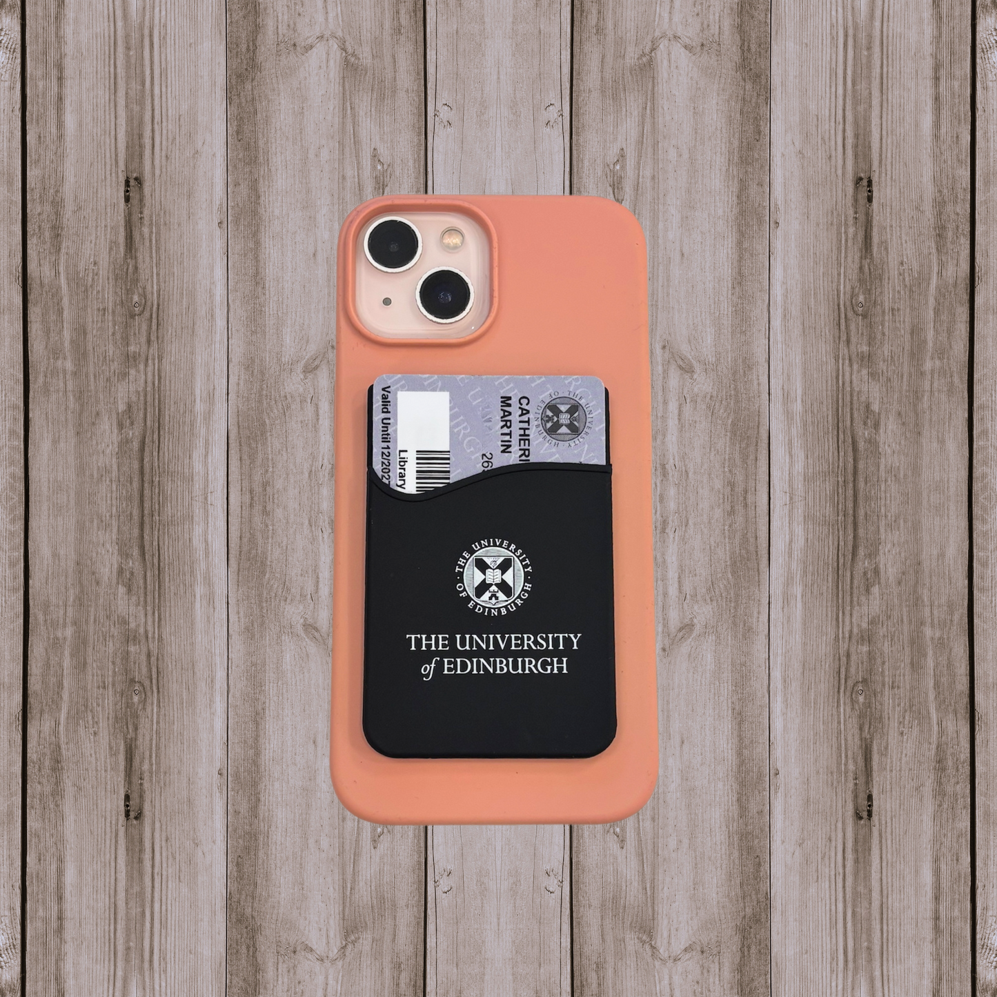 Black silicone phone wallet with white university crest logo designed to securely hold cards. The wallet is slim, adhesive-backed, and attaches to the back of a phone or phone case for easy access.