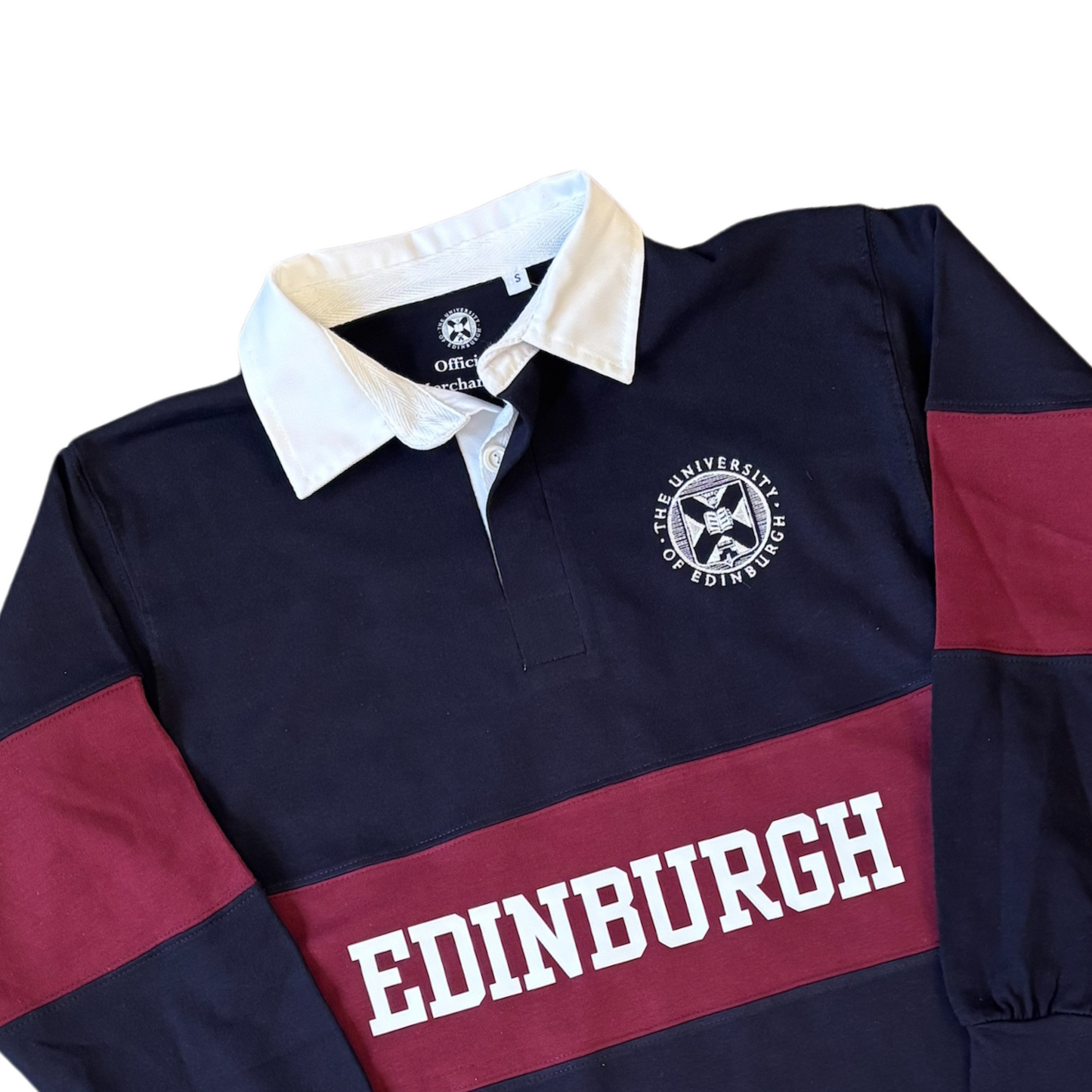 A closer look at our navy blue and maroon varsity rugby shirt featuring a white collar and a two-button placket. The shirt has a bold maroon horizontal stripe across the chest with "EDINBURGH" printed in white capital letters. On the upper left chest area, there is a circular embroidered emblem of the University of Edinburgh. The long sleeves have matching maroon panels on the upper arms, and the cuffs are ribbed.
