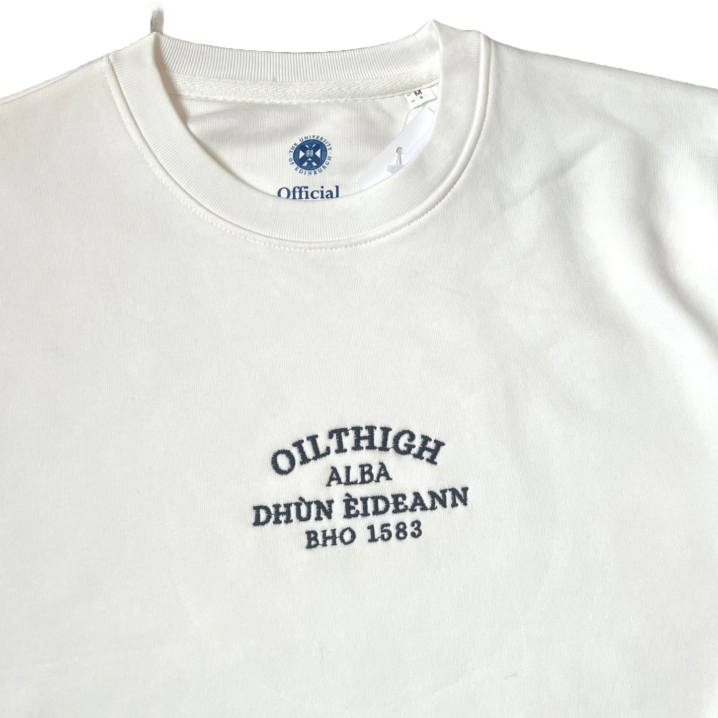 CLose up of Off white sweatshirt with 'Oilthigh Dunn EIdean, bho 1583, Alba" embroidered in black