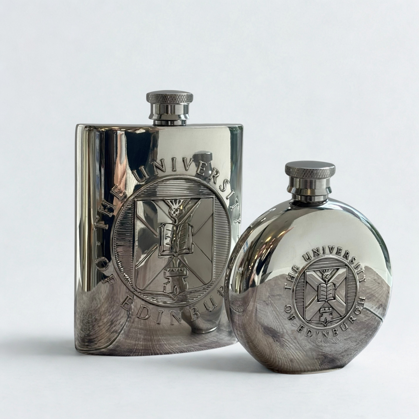 The 6 oz square hip flask next to the 4 oz round hip flask.