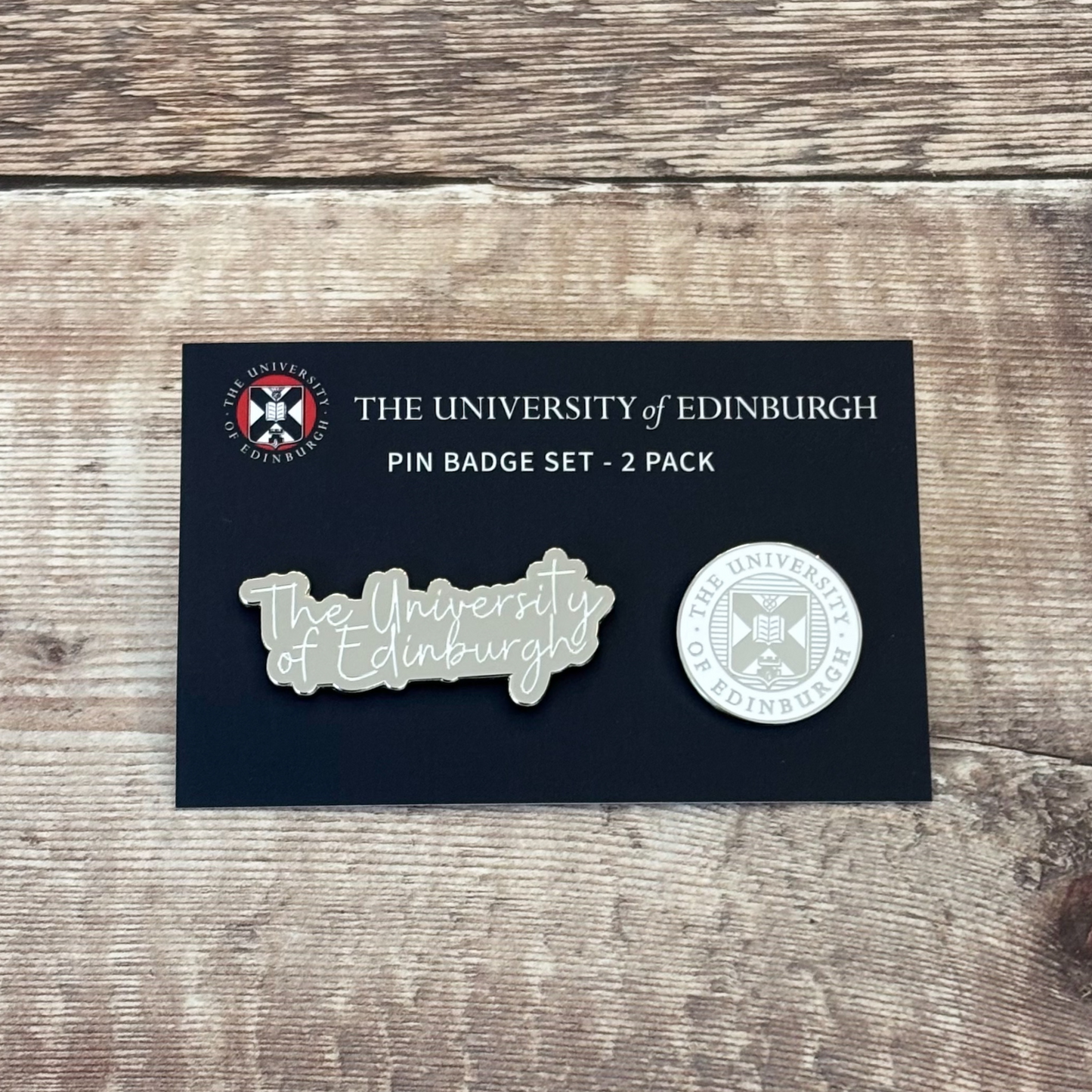 Two silver and white pins on a navy backing card. The pin on the left says 'University of Edinburgh' in a calligraphy-style font. The pin on the right is the University crest.