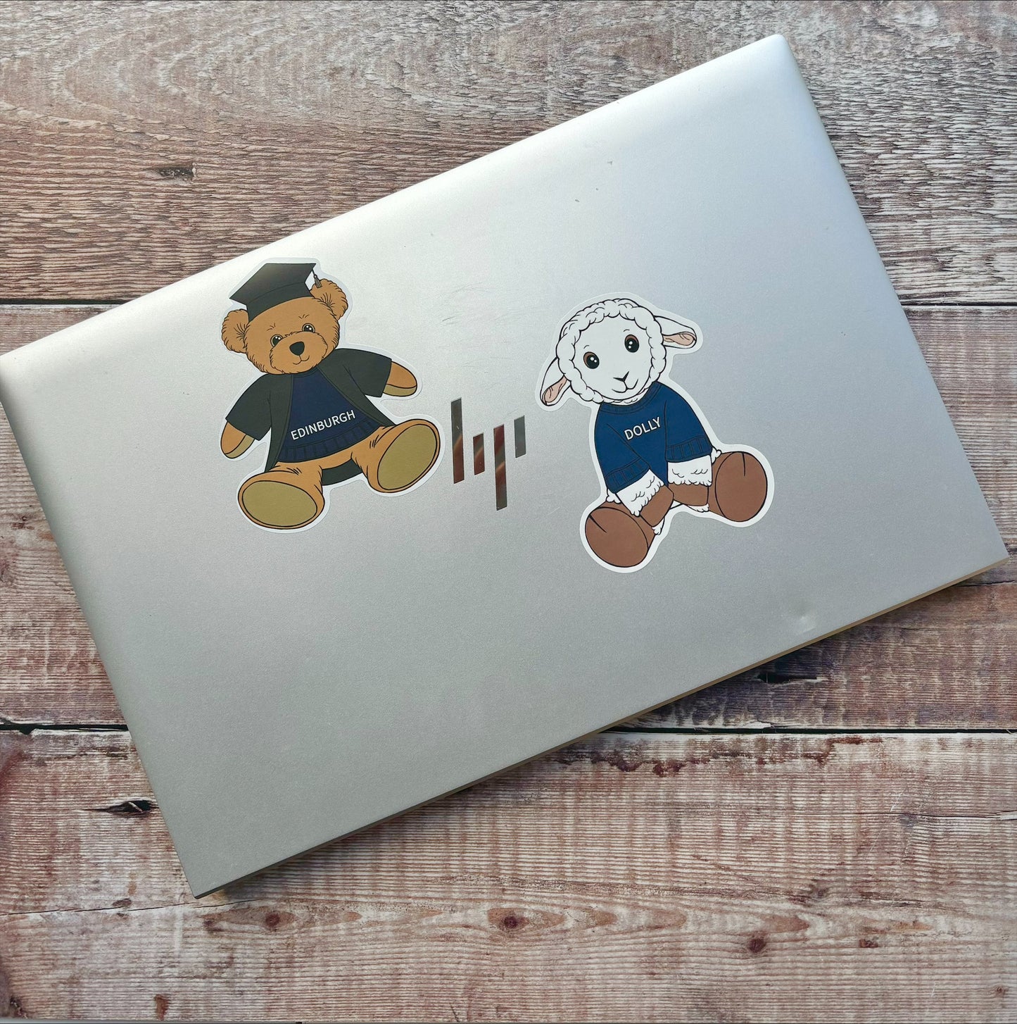 Edinbear teddy in graduation gown and Dolly the Sheep laptop stickers on laptop. Art by Sara Julia Campbell.