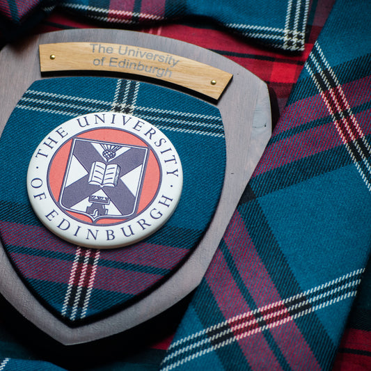 Wall plaque with dark wood featuring university tartan, university crest and engrave plate saying 'The University of Edinburgh', pictured next to tartan tie