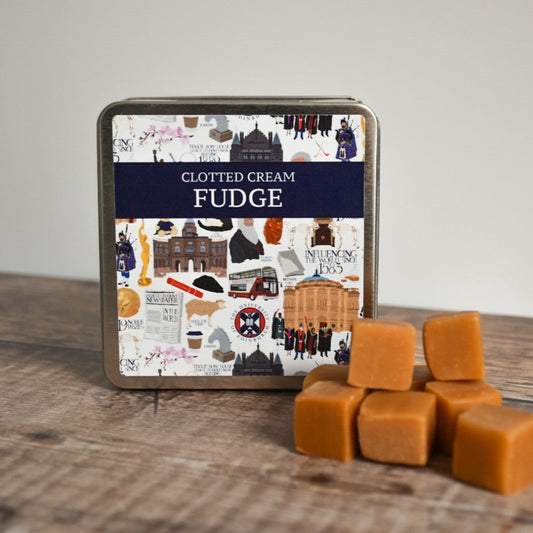 Clotted Cream Fudge tin container propped up. Small stack of fudge squares arranged in front of the tin.