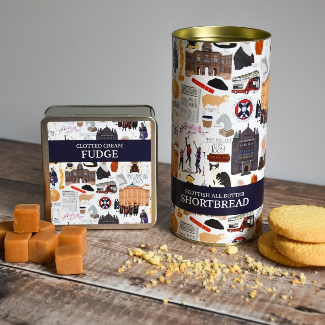 Clotted Cream Fudge and Scottish All Butter Shortbread tin containers positioned side by side. They have illustrations of the University of Edinburgh on them. Stacks of fudge and shortbread cookies are arranged to their sides.
