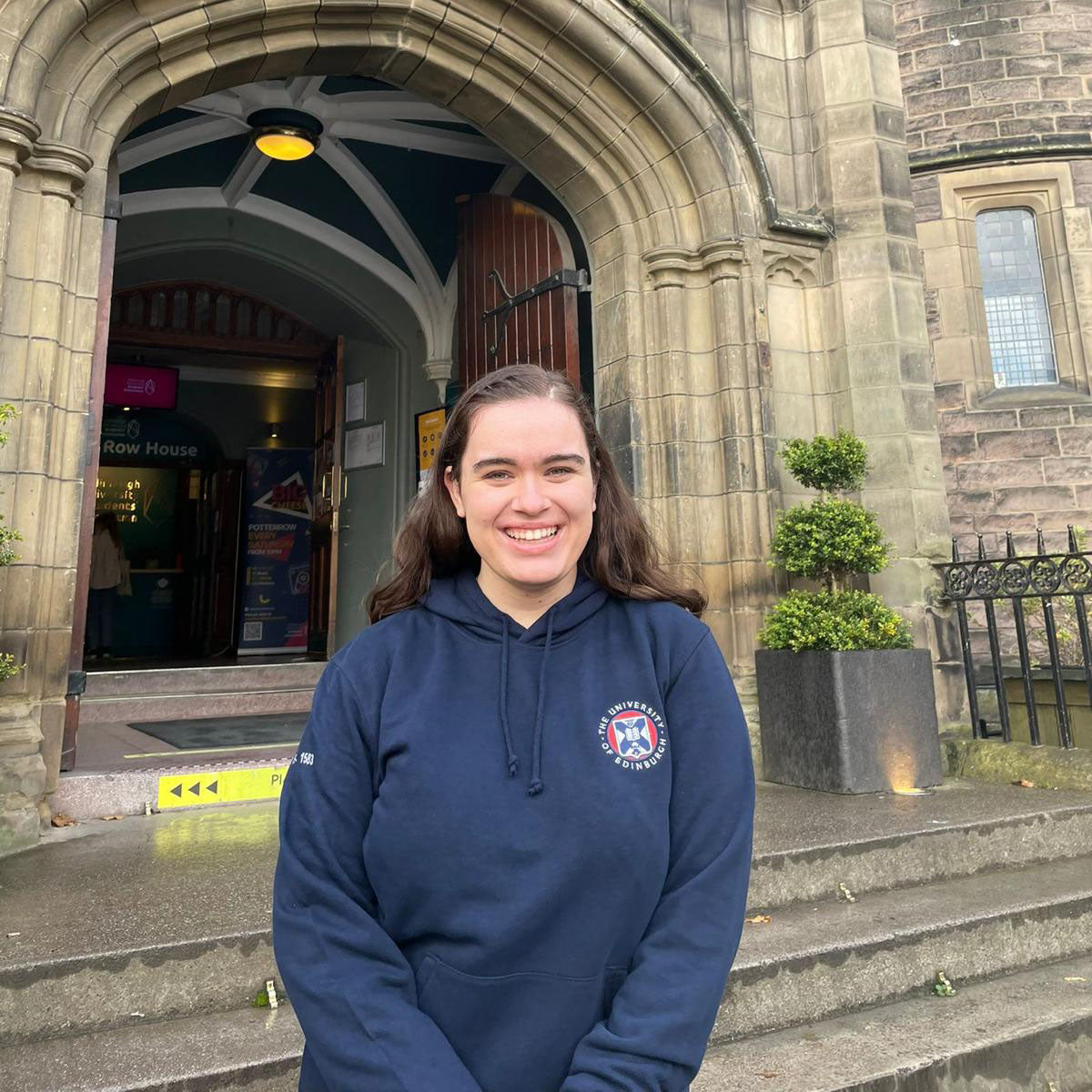 A photo of one of our models wearing the Embroidered Logo Hoodie outside of Teviot Row House.