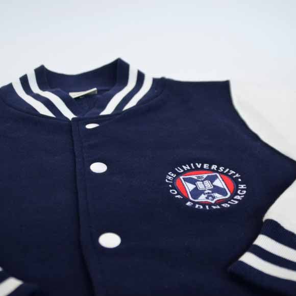 Close up of Navy Varsity Style Baseball Jacket with white contrast sleeves, white buttons and University crest details.
