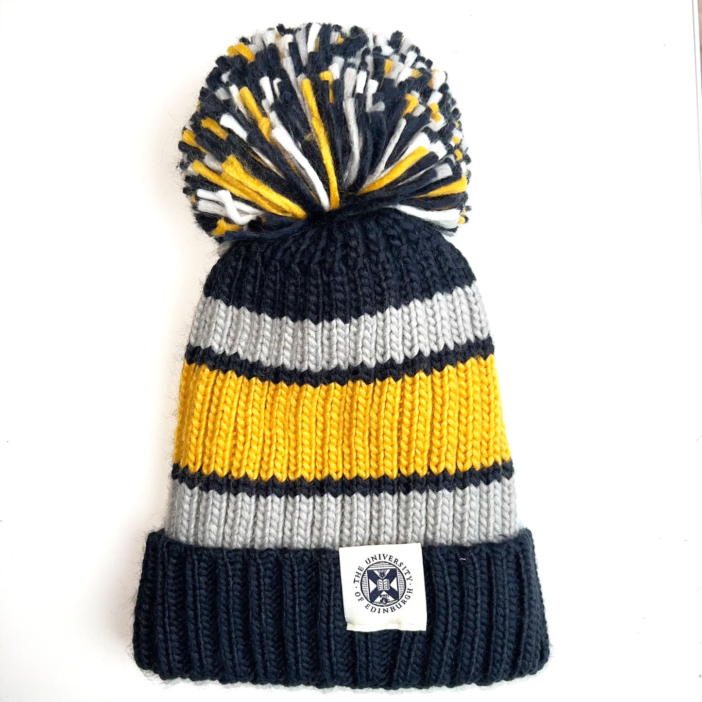 Ribbed knit pom pom hat with grey and yellow striping and pom pom detailing.