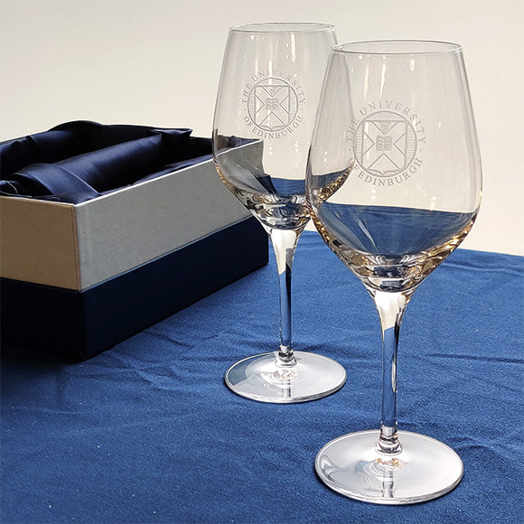 A pair of crystal wine glasses with University crest etching displayed in front of a presentation box.