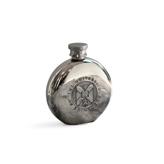 Front view of the round pewter hip flask with the embossed University crest visible.
