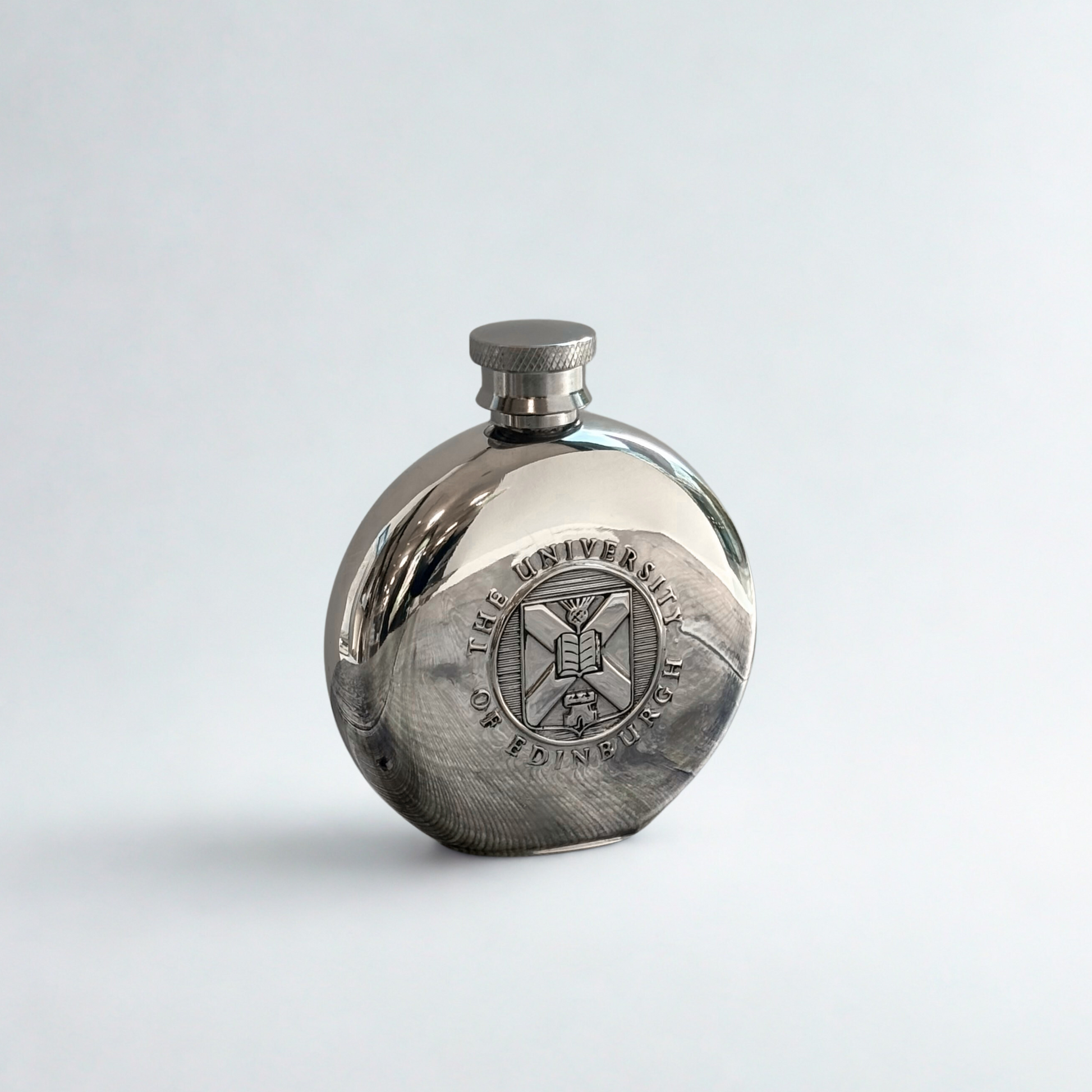 Front view of the round pewter hipflast with the embossed University crest visible.