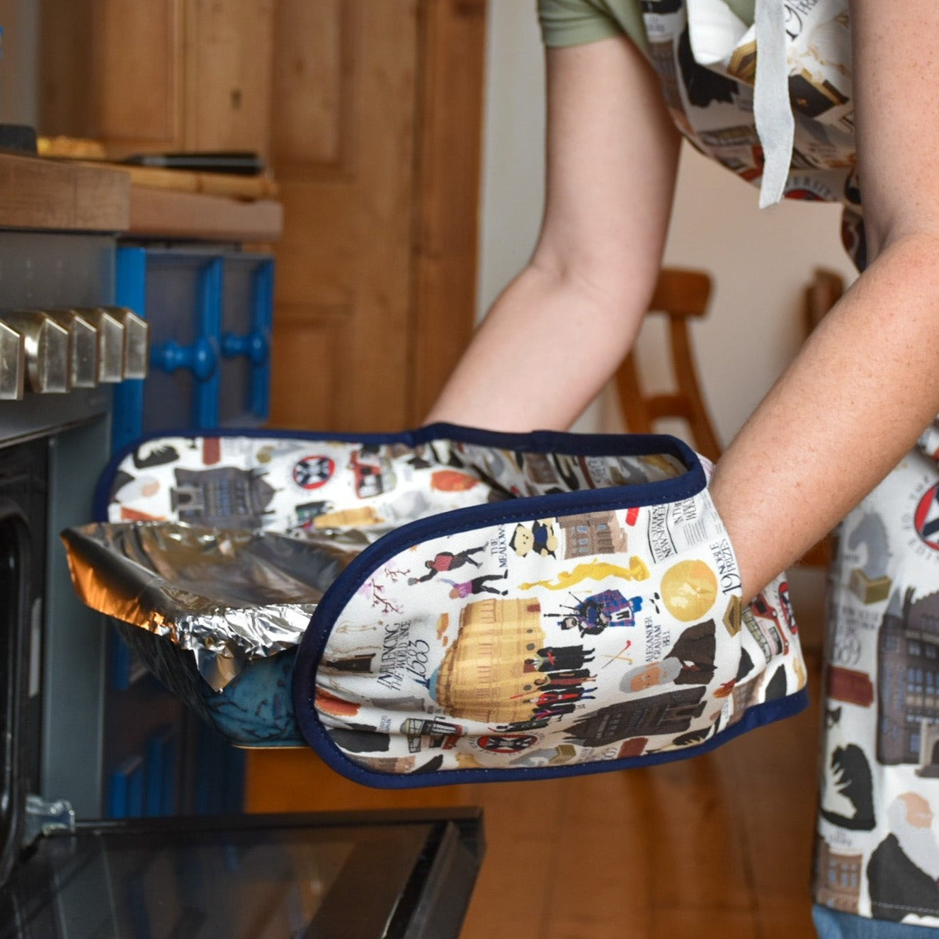Model uses oven gloves with illustrations of various University of Edinburgh icons, buildings, and figures.