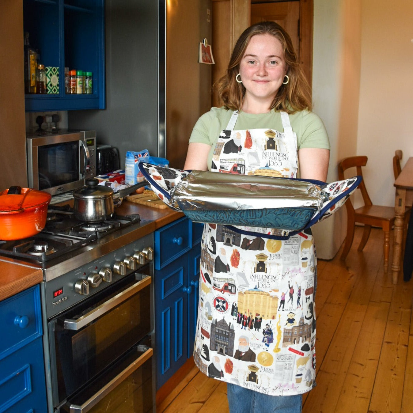 Model wears apron and oven gloves with illustrations of various University of Edinburgh icons, buildings, and figures.