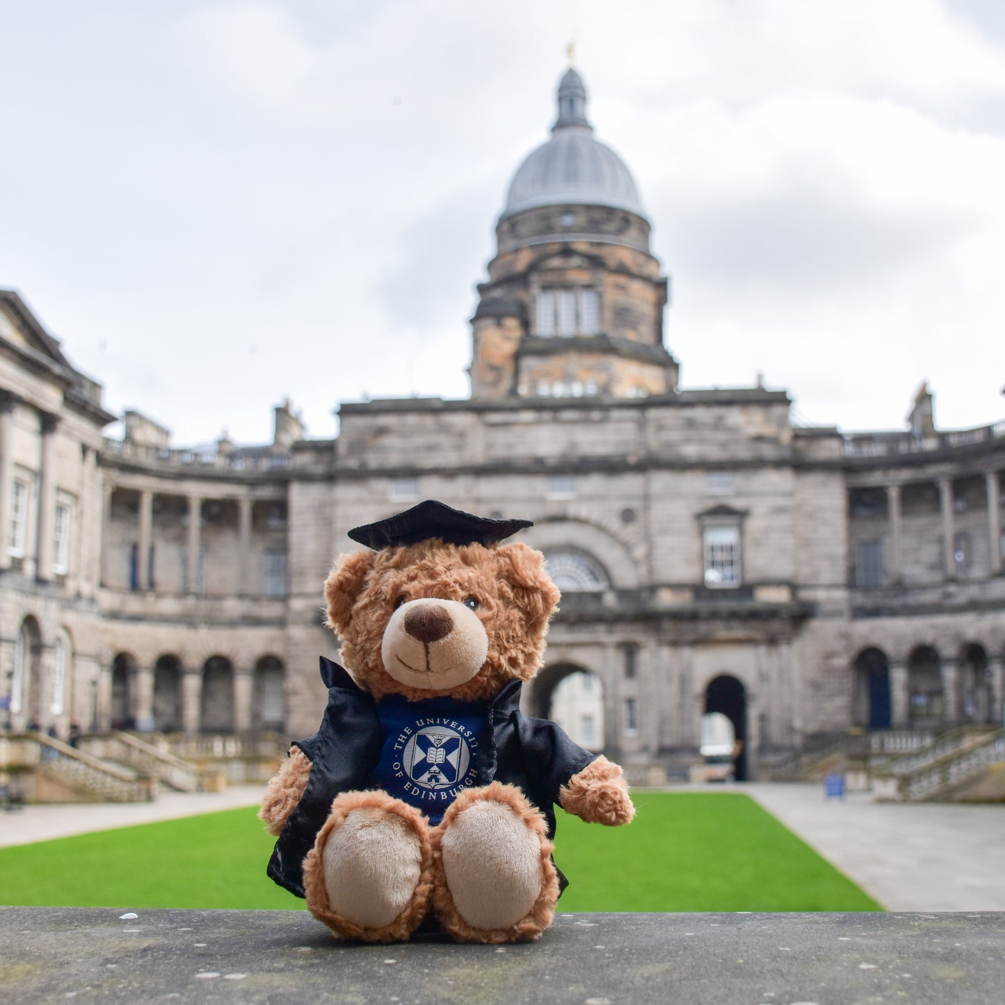 Edinbear Recycled Plush sitting in front of the Old College quad and Golden Boy statute.