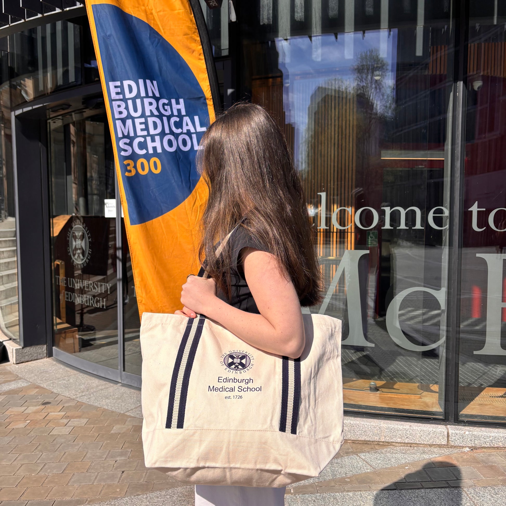 Person holding a tote bag with Edinburgh Medical School branding in front of a building entrance.