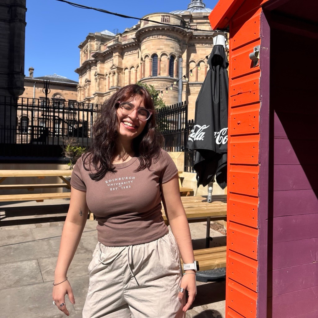Model wears brown cropped and fitted t-shirt with 'Edinburgh University EST. 1583' text in the Teviot garden