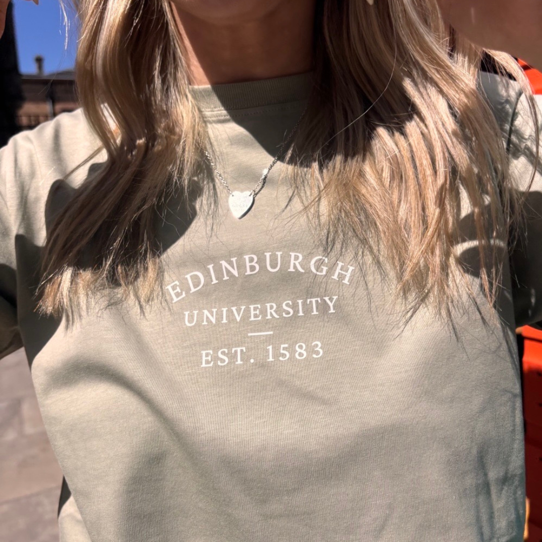 Person wearing light olive Everyday T-Shirt with 'Edinburgh University EST. 1583' text.