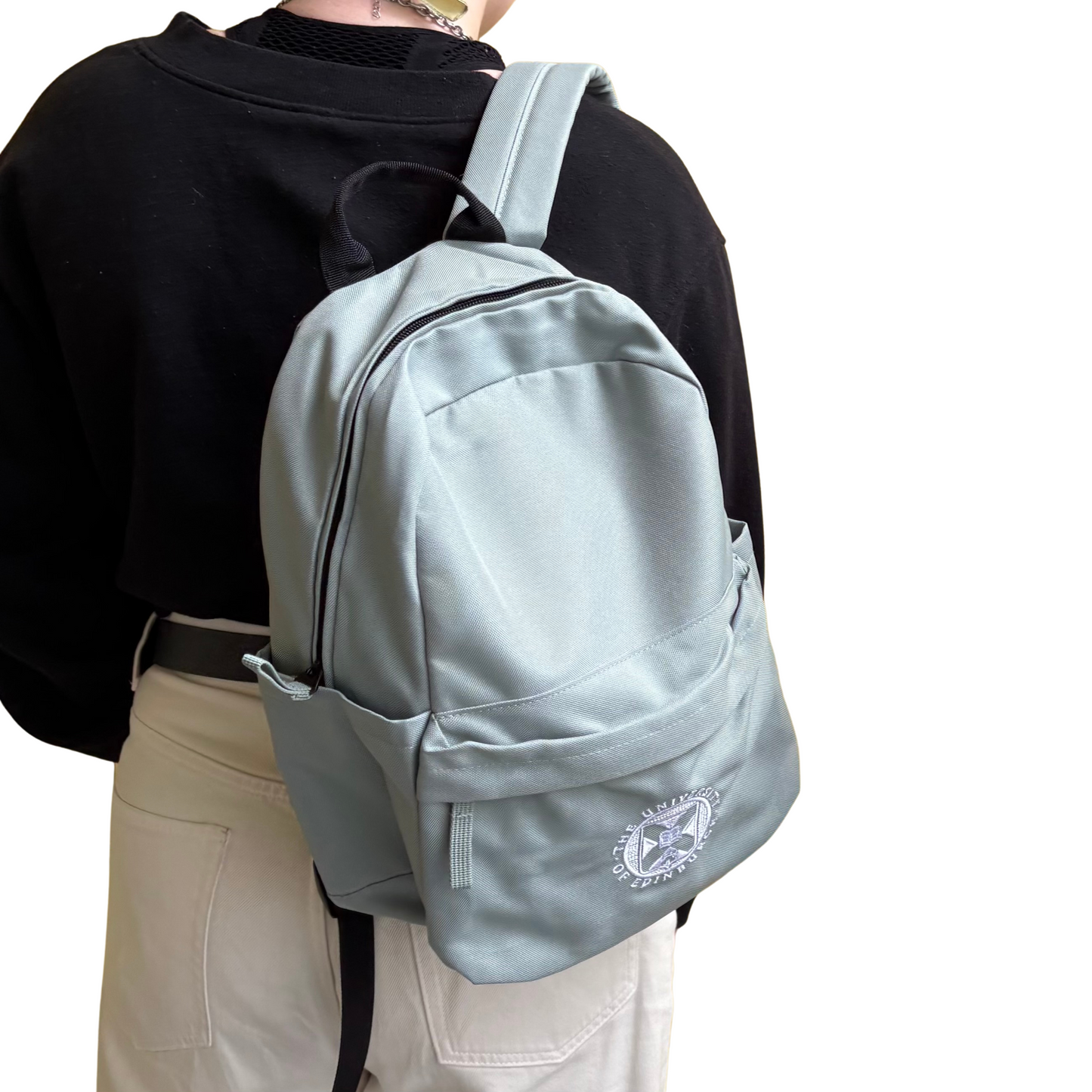 Model wears the Mini Recycled Crest Backpack in dusty green featuring the University crest embroidered in white.