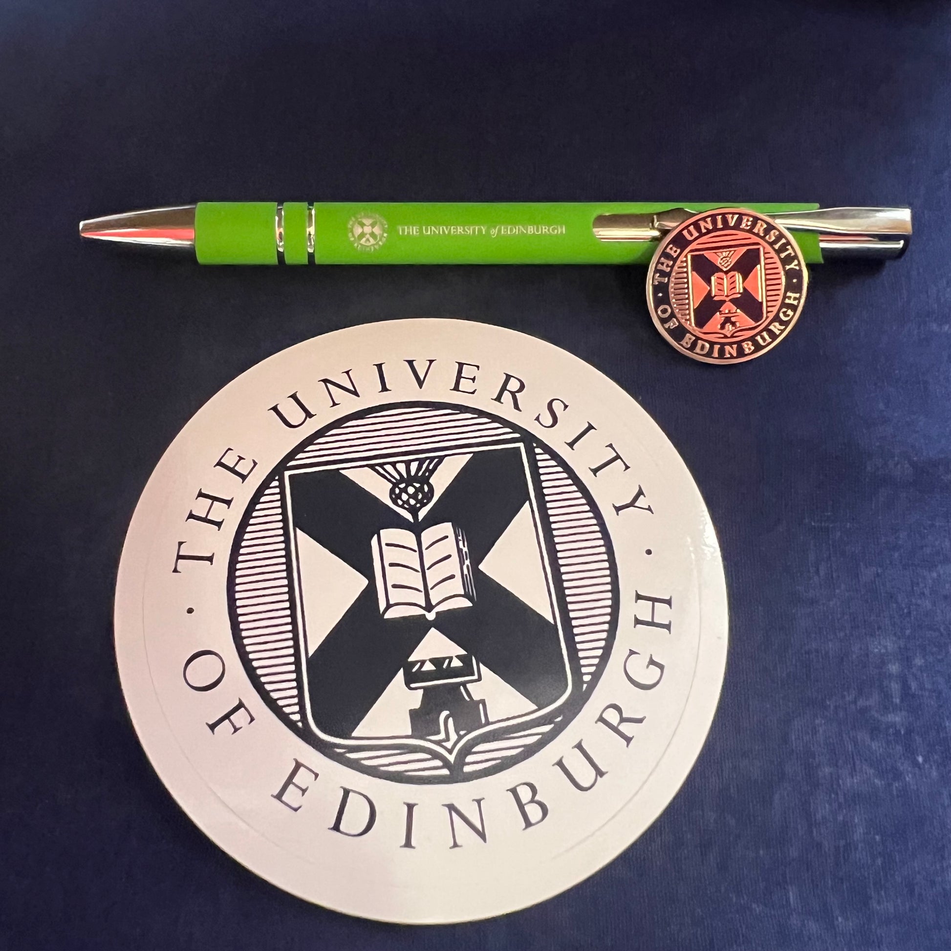 Green pen, navy and silver crest pin badge, navy and white university crest sticker