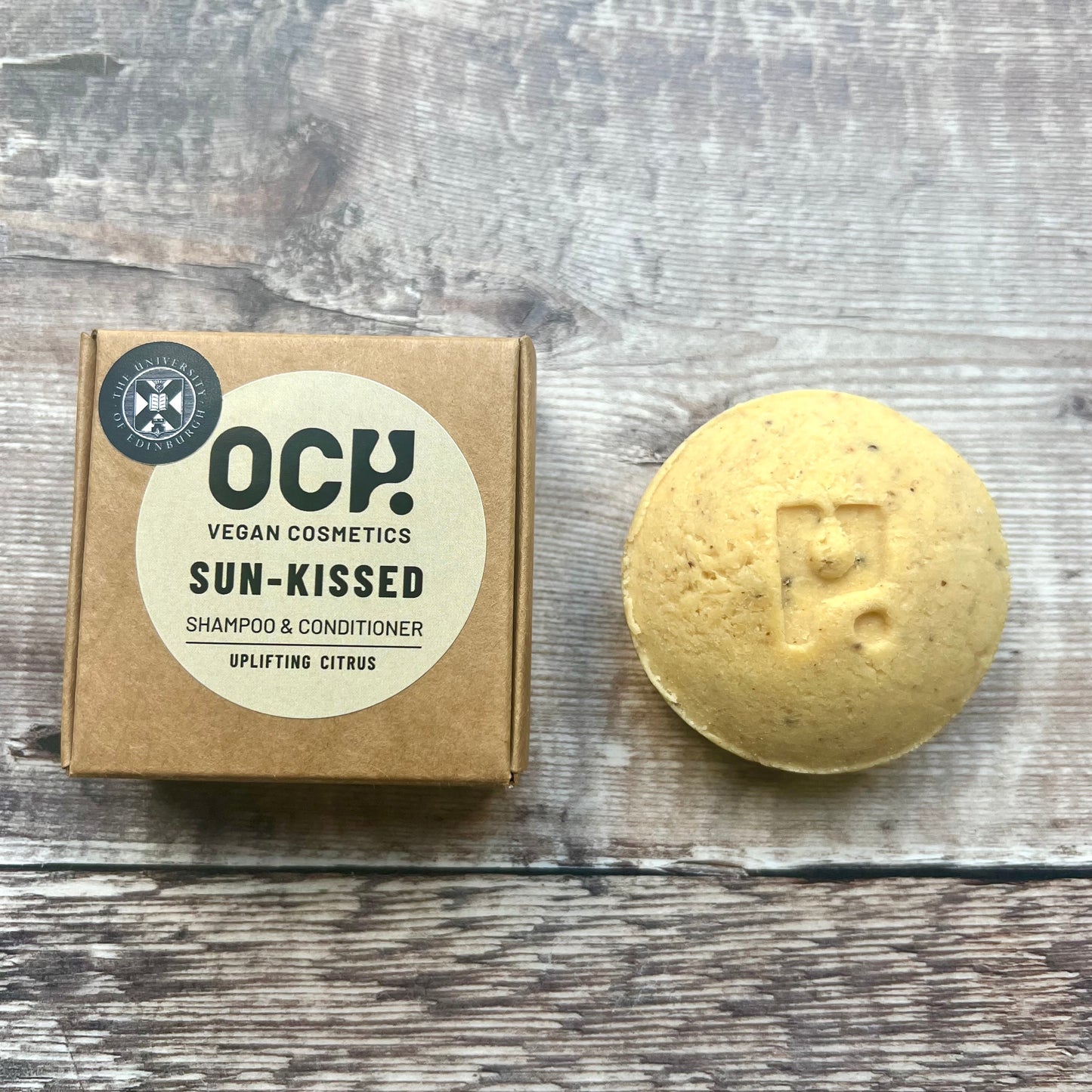 ROUND yellow shampoo bar next to brown paper box featuring universitycrest