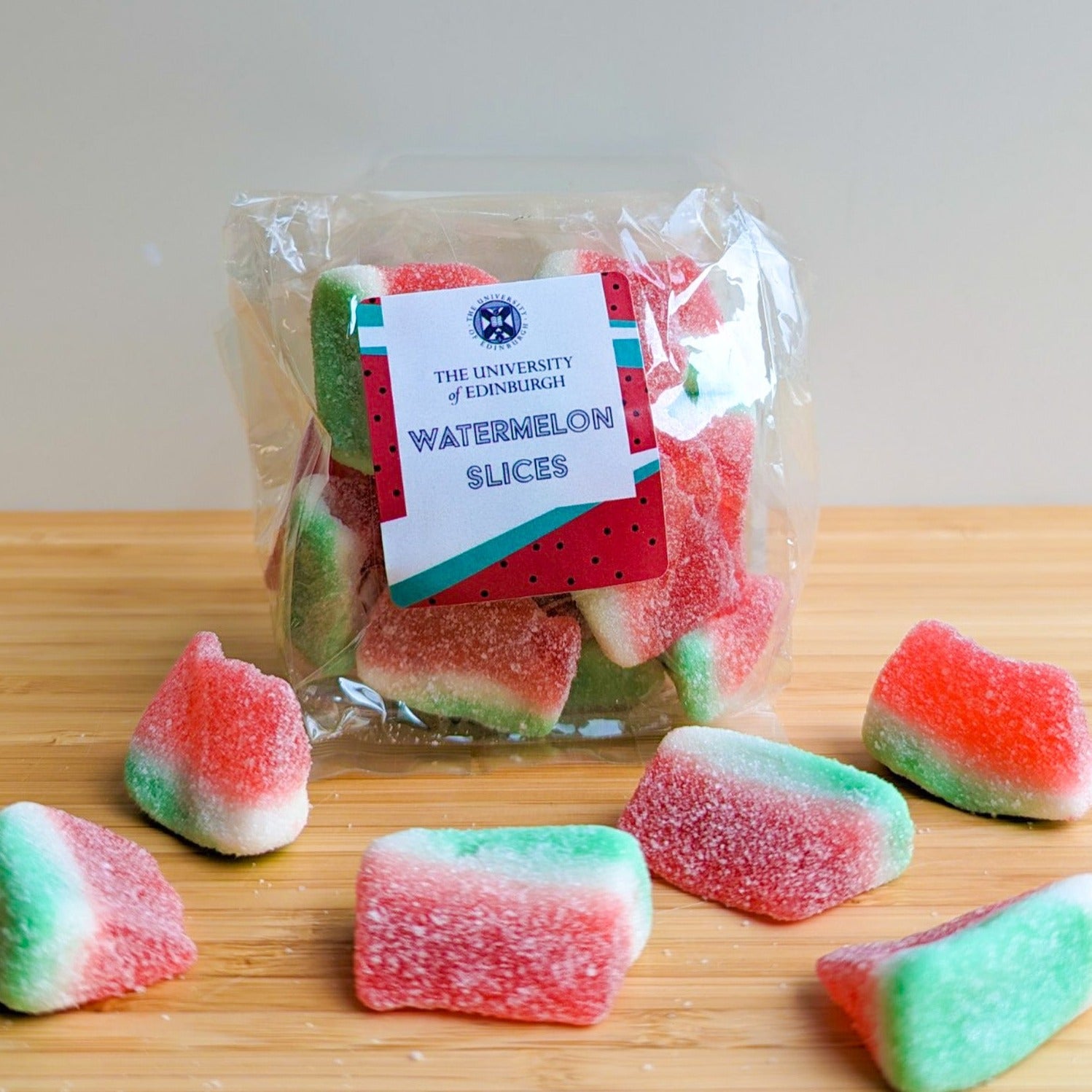 Close up of a plastic bag of Watermelon Slice candies. A few candies are scattered in front of the bag. The University of Edinburgh's Crest is on the candy label.