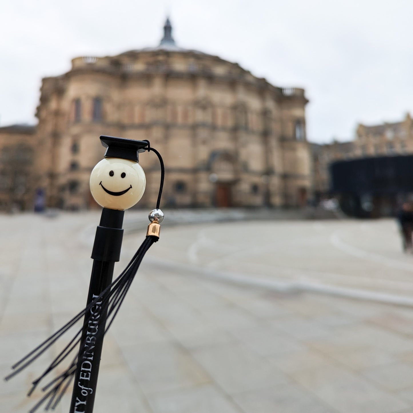 novelty pen featuring a smiling face and a black graduation cap with a tassel in front of McEwan Hall