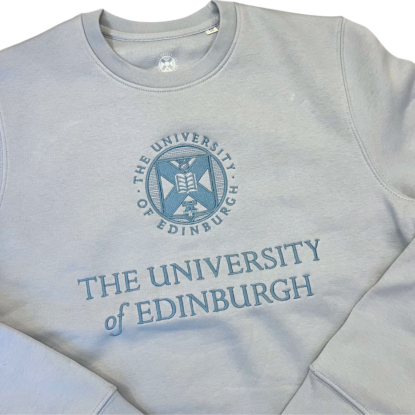 close up of blue embroidered university crest and name on the light blue tonal crewneck sweatshirt