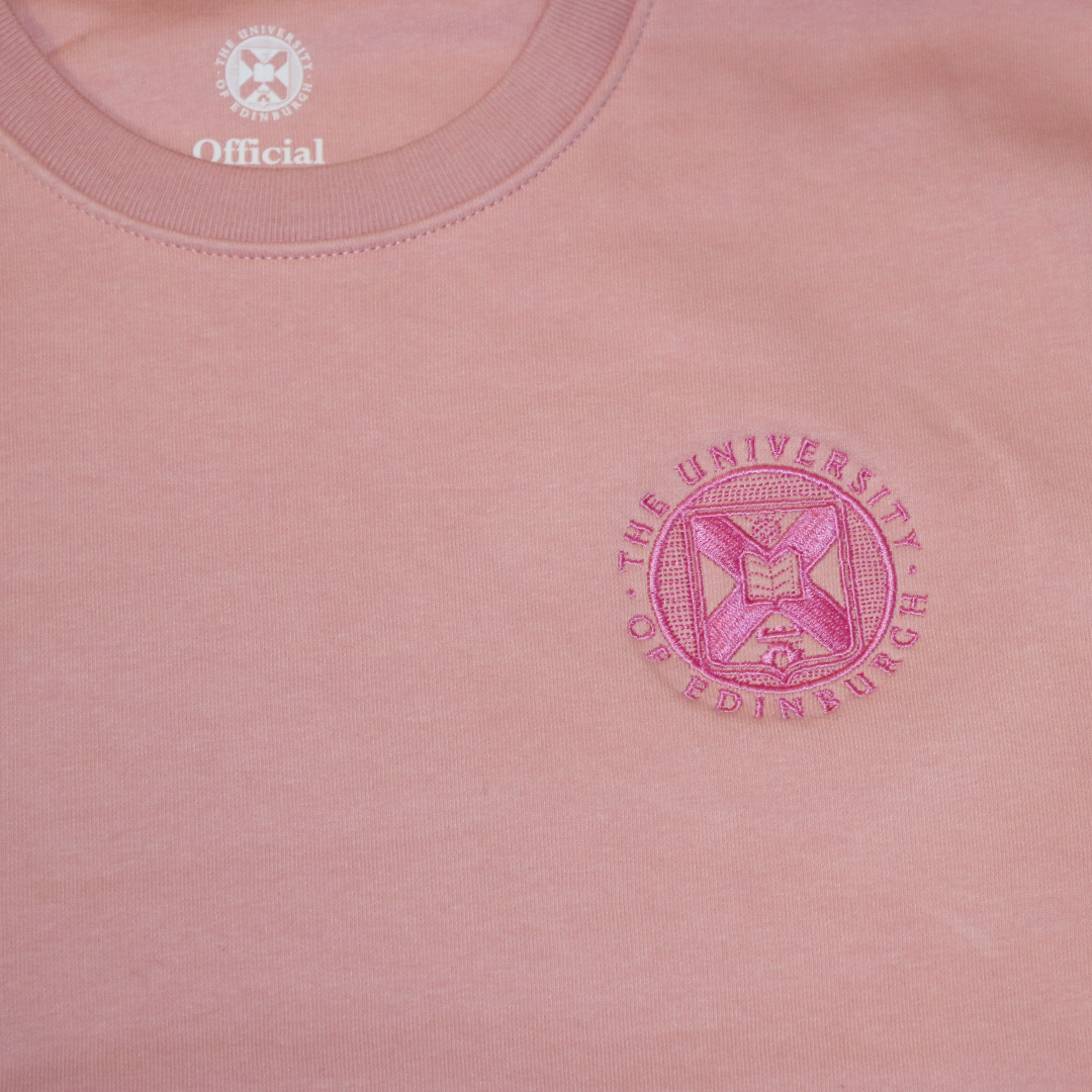 close up of the shiny pink embroidered university crest on the upper right chest area of the pink tonal crewneck sweater