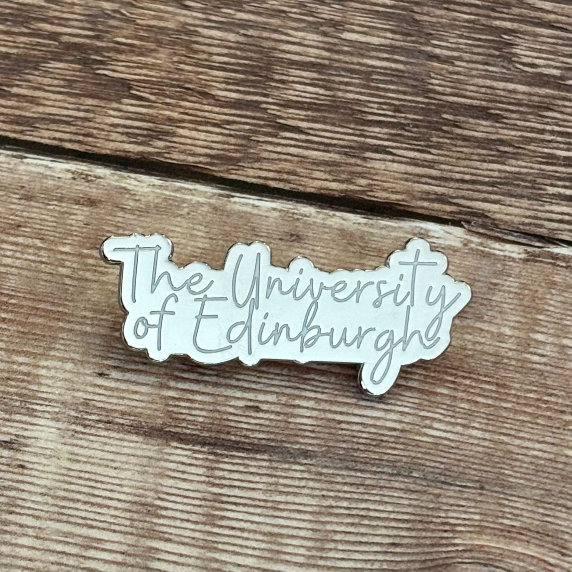 Silver and white 'University of Edinburgh pin badge'.