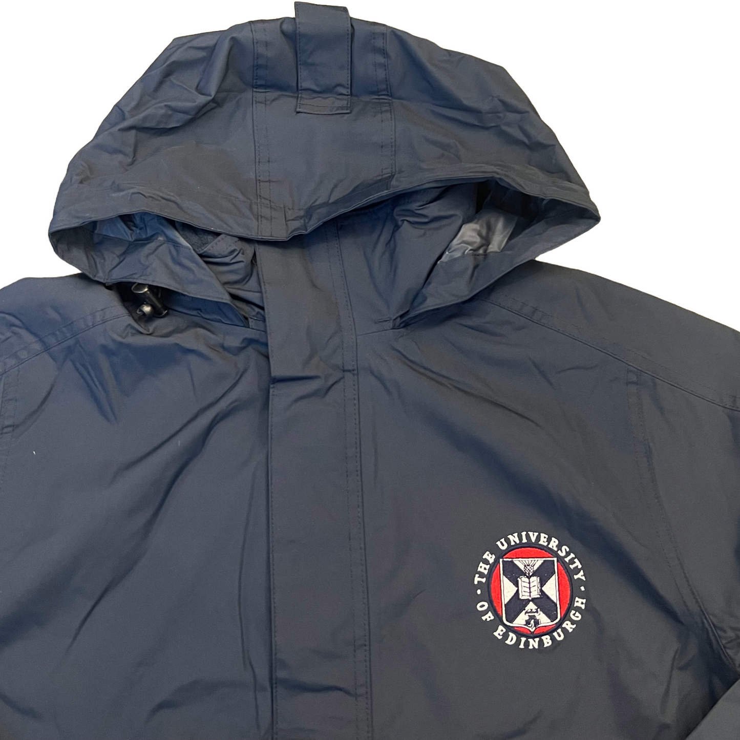 navy waterproof jacket with hood up,  with the University crest embroidered on the left chest in white, red and navy 