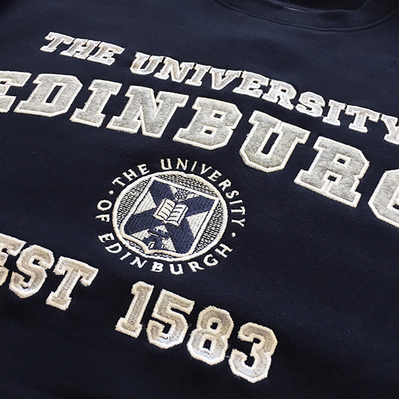 Detail of the appliqué in Our Premium Applique Sweatshirt in navy. It features applique 'The University of Edinburgh, Est 1583' detail and University crest.
