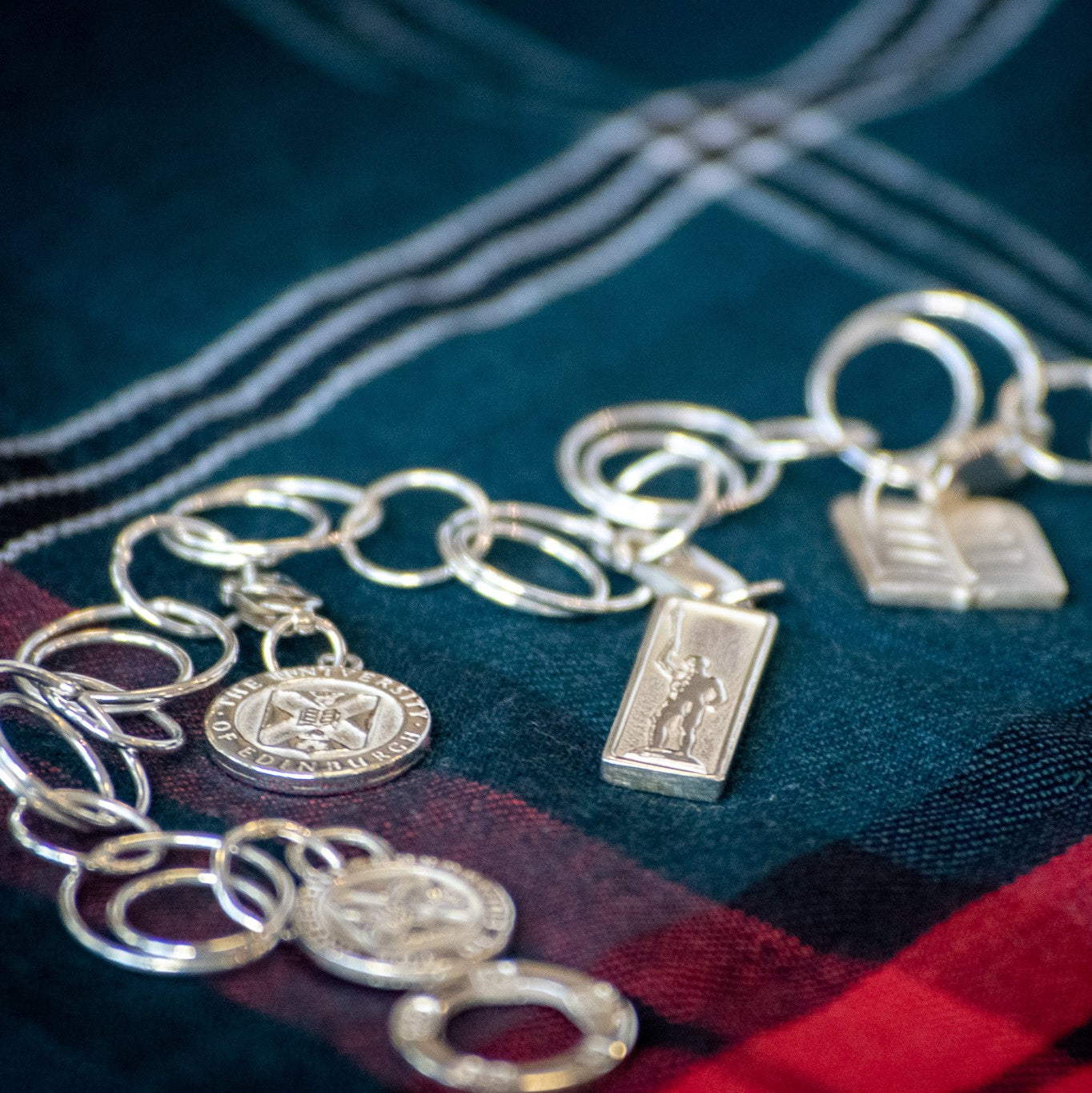 Our Silver Charm bracelet with Crest, Golden Boy and Book charms on a University Tartan background.