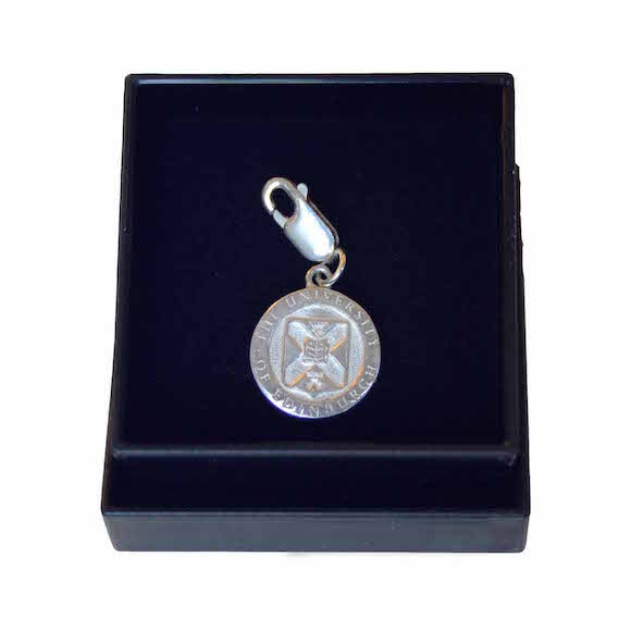 A silver charm featuring the Edinburgh University Crest  in a black box with black velvet lining.