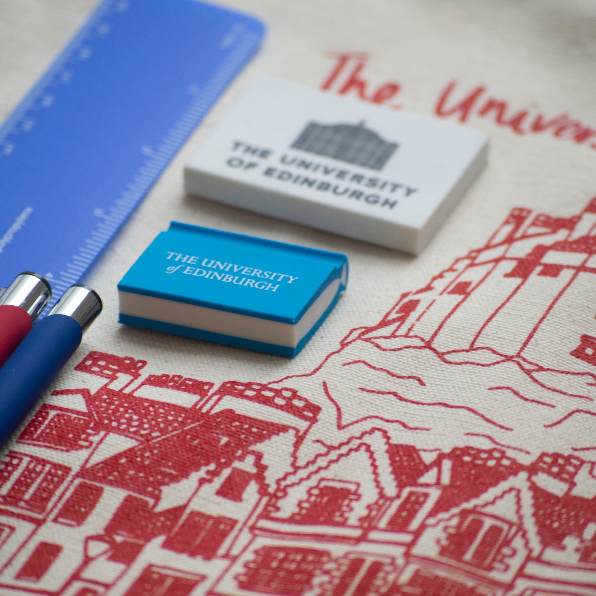 Our soft feel pens in red and blue as well as our blue flexible ruler, blue book eraser and McEwan hall eraser on a background of our Edinburgh castle tote bag. 