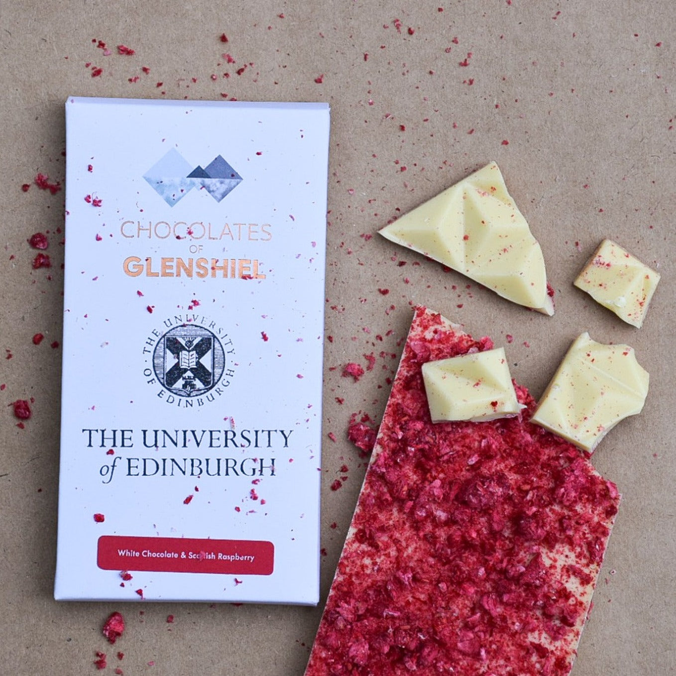 White chocolate bar with a raspberry top coating broken into pieces displayed next to its package