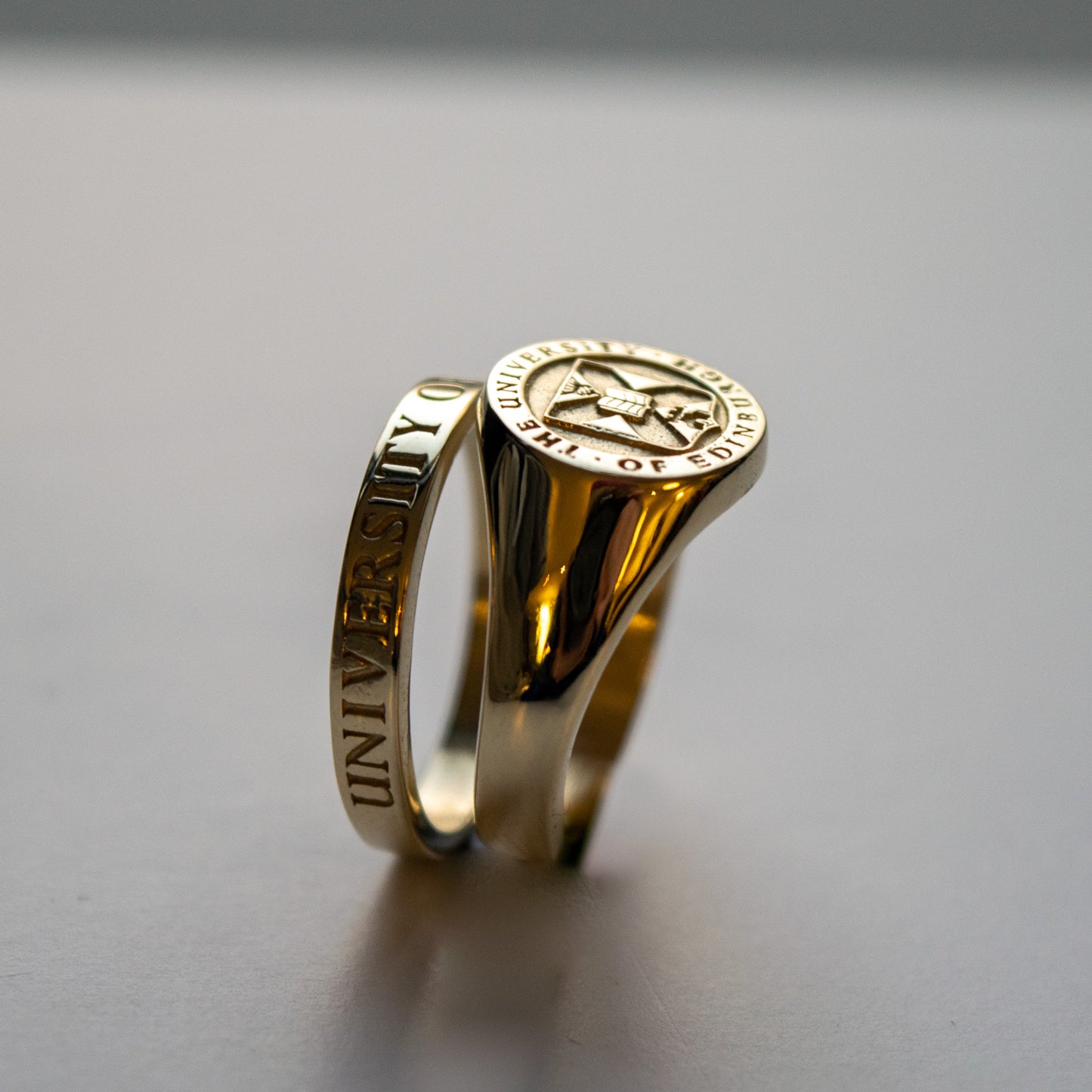 Gold graduation Signet Ring featuring the University crest with thin gold band ring bhind