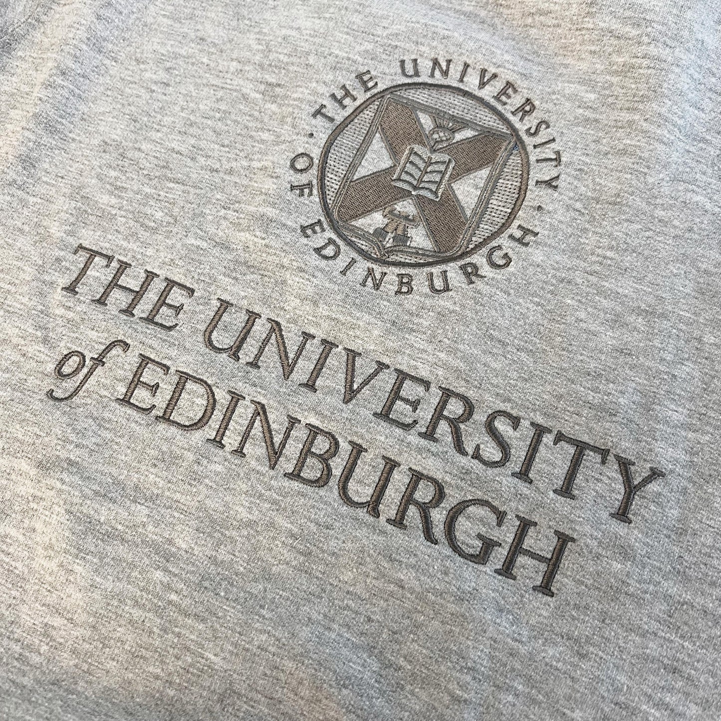 Close up image of the tonal embroidery of the University crest on a grey sweatshirt
