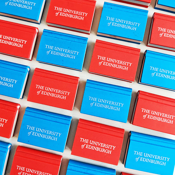 Two book shaped erasers, one in red and one in blue, with University branding in white in a recurring pattern. 