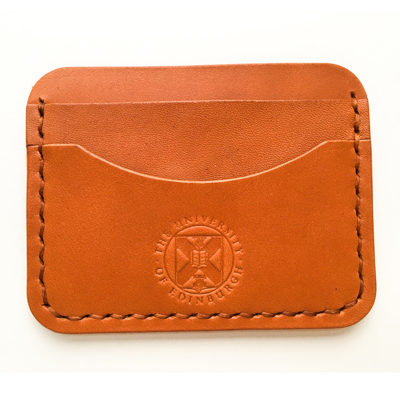 Close up of the tan Leather Card Holder demonstrating the stitching detail and the embossed crest. 