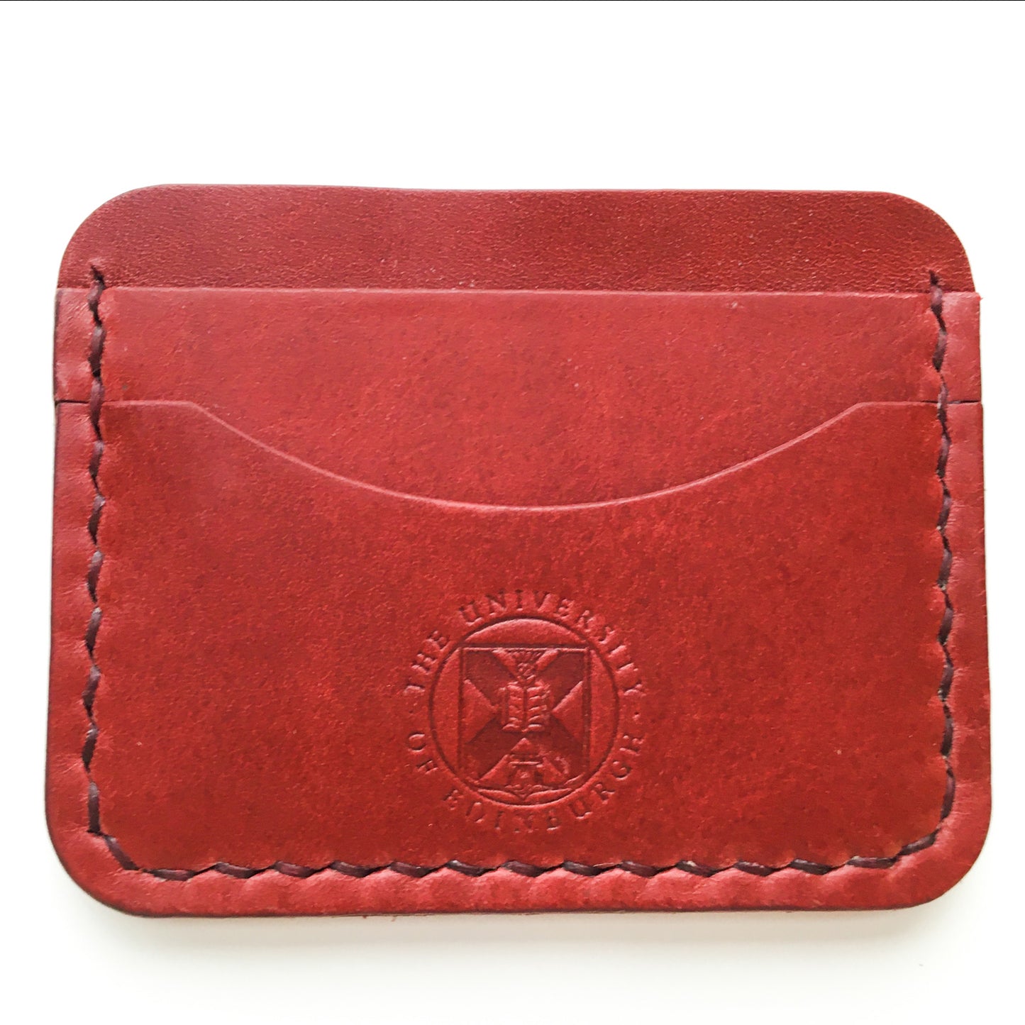Close up of the red Leather Card Holder demonstrating the stitching detail and the embossed crest. 